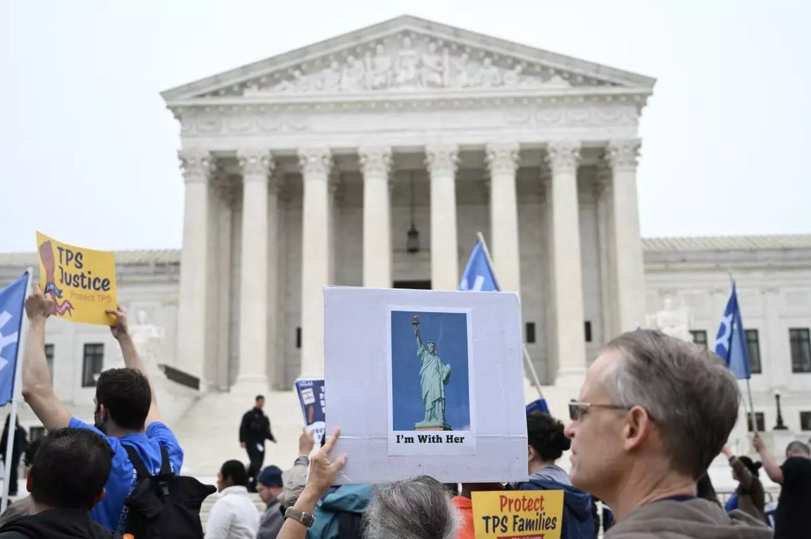 Protesters hold signs outside the U.S. Supreme Court building, including messages supporting Temporary Protected Status and a sign reading “I’m With Her” with an image of the Statue of Liberty.