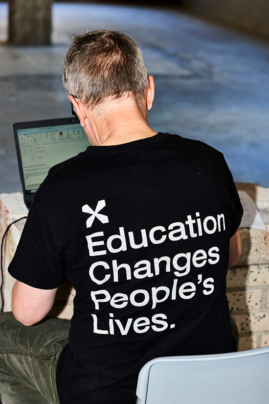 Midrange shot from back of person wearing black shirt with "Education changes people's lives" in white lettering