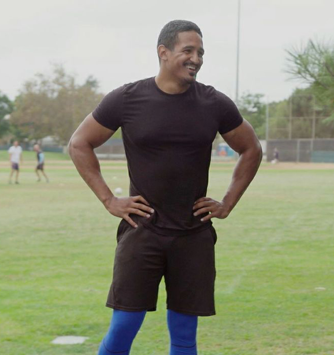 Man in black T-shirt and shorts standing on a field with hands on hips
