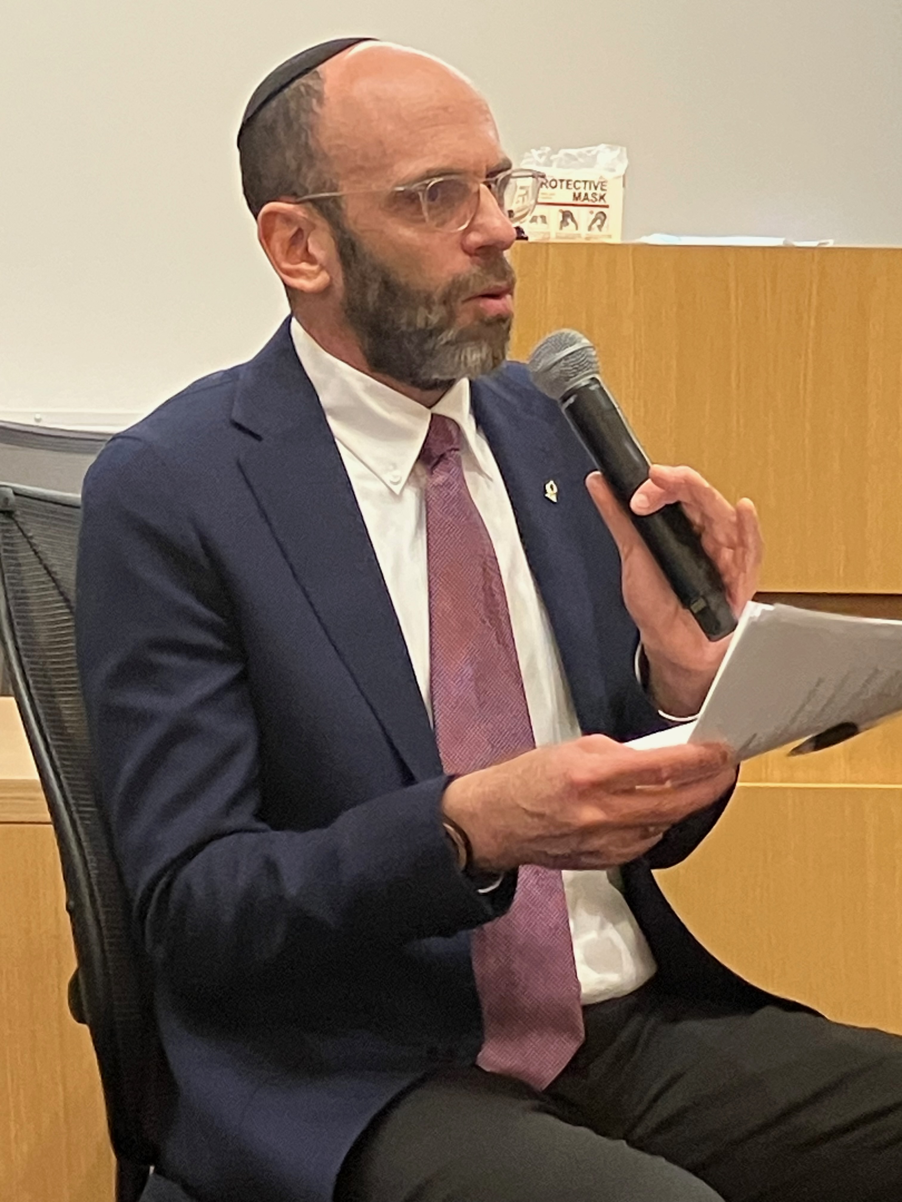 Dr. Matthew Fox seated, holding sheet of paper and speaking into microphone