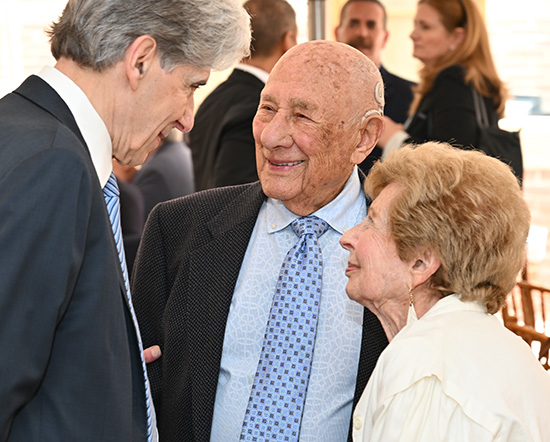 Julio Frenk, left, in dark suit, speaks with Meyer Luskin, in blue shirt and dark jacket, and Renee Luskin, in white top
