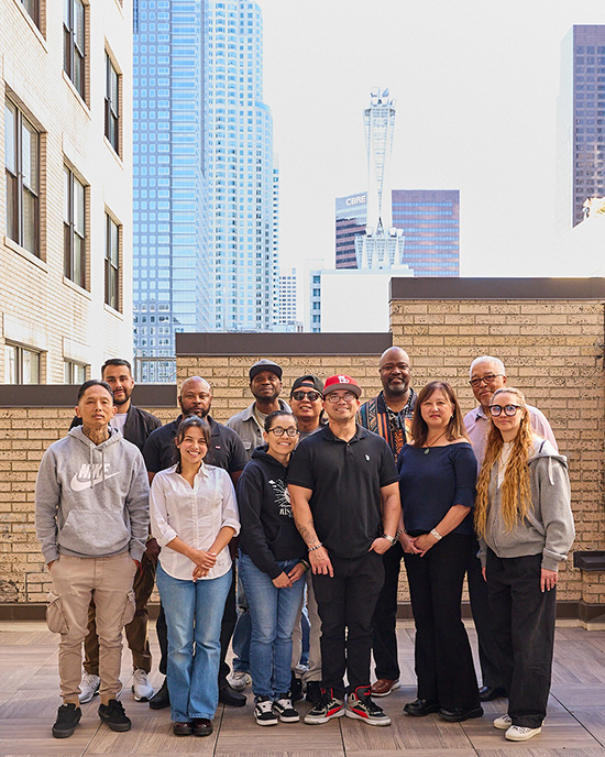 A group of 12 people posing in front of a tan brick wall; Taffany Lim is third from the right