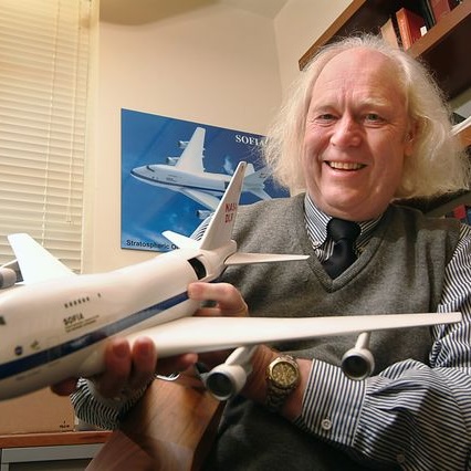 Close shot of Eric Becklin in gray cardigan and blue tie holding a model airplane.