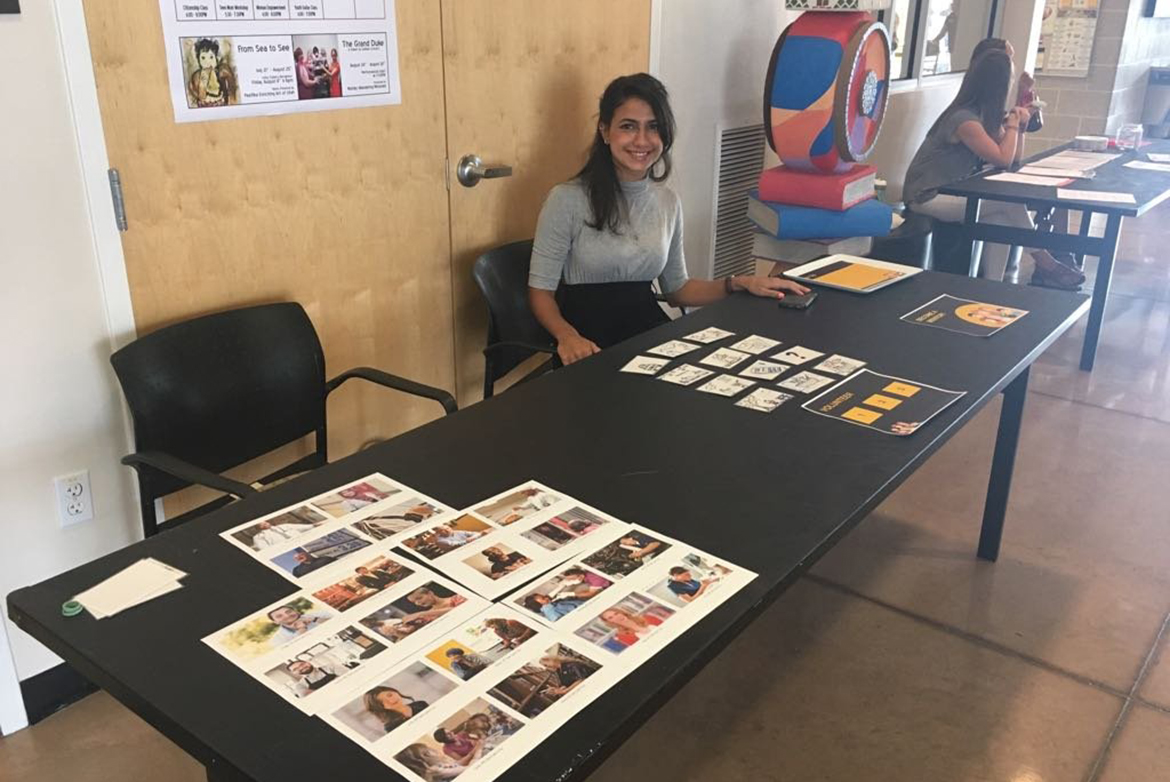 Far shot of Salma Mousa sitting at a table with photos and cards on it