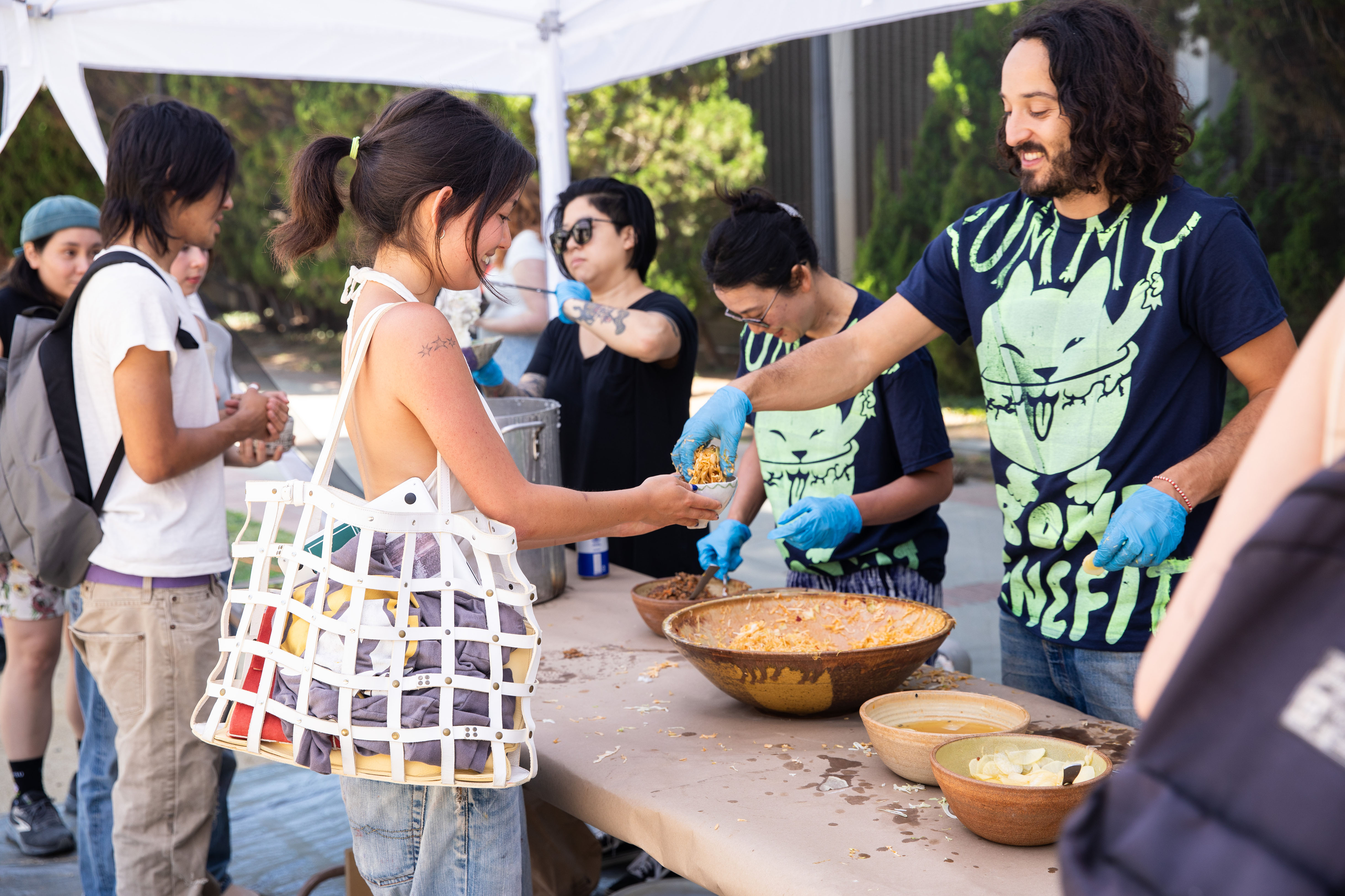 A person wearing a Yummy Bowl Benefit T-shirt fills a bowl held out by a woman.