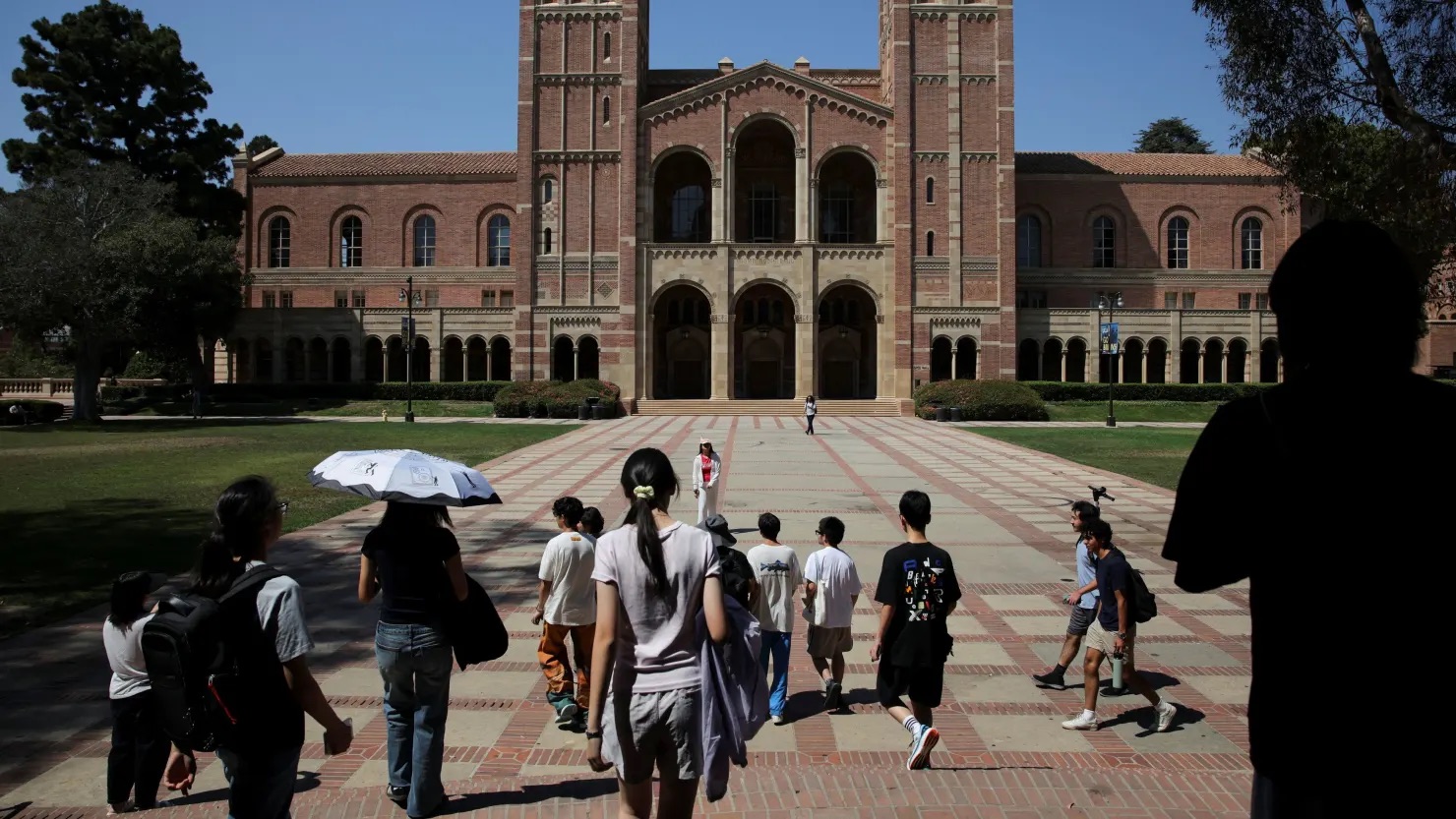 Students walk across UCLA’s Royce Quad toward Royce Hall on a sunny day, with the brick Romanesque building rising in the background.