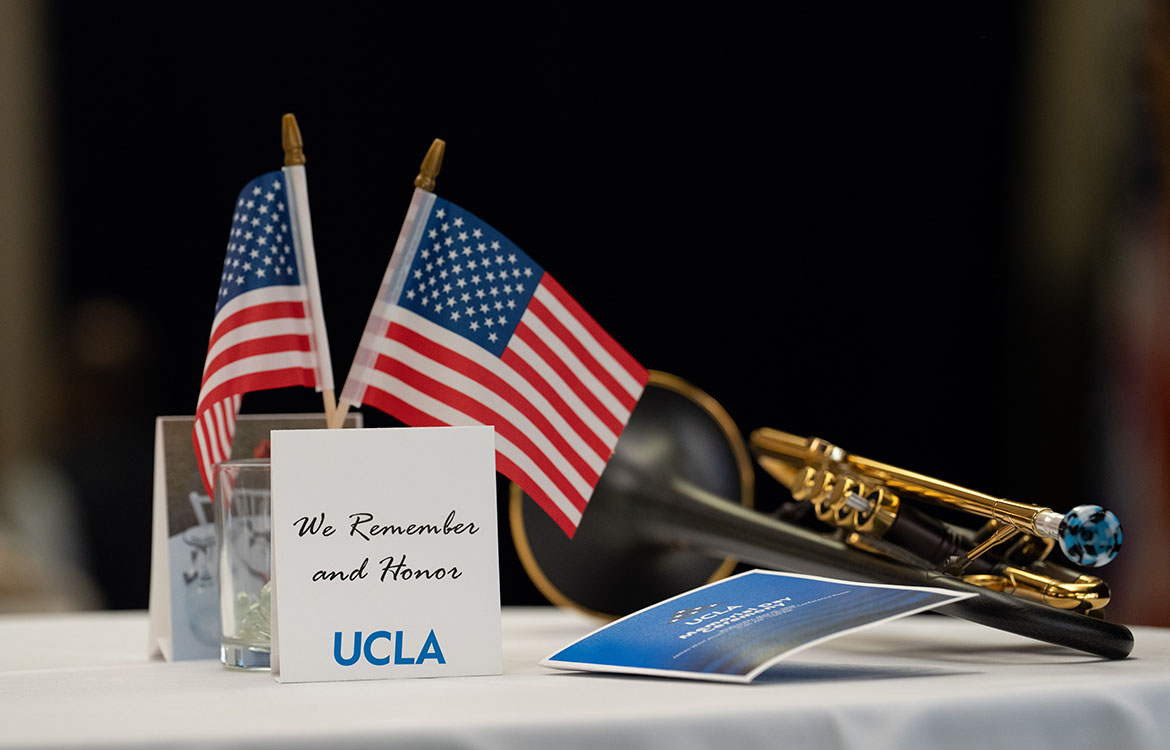 A table display with two small American flags, a card reading "We Remember and Honor – UCLA," and a trumpet.