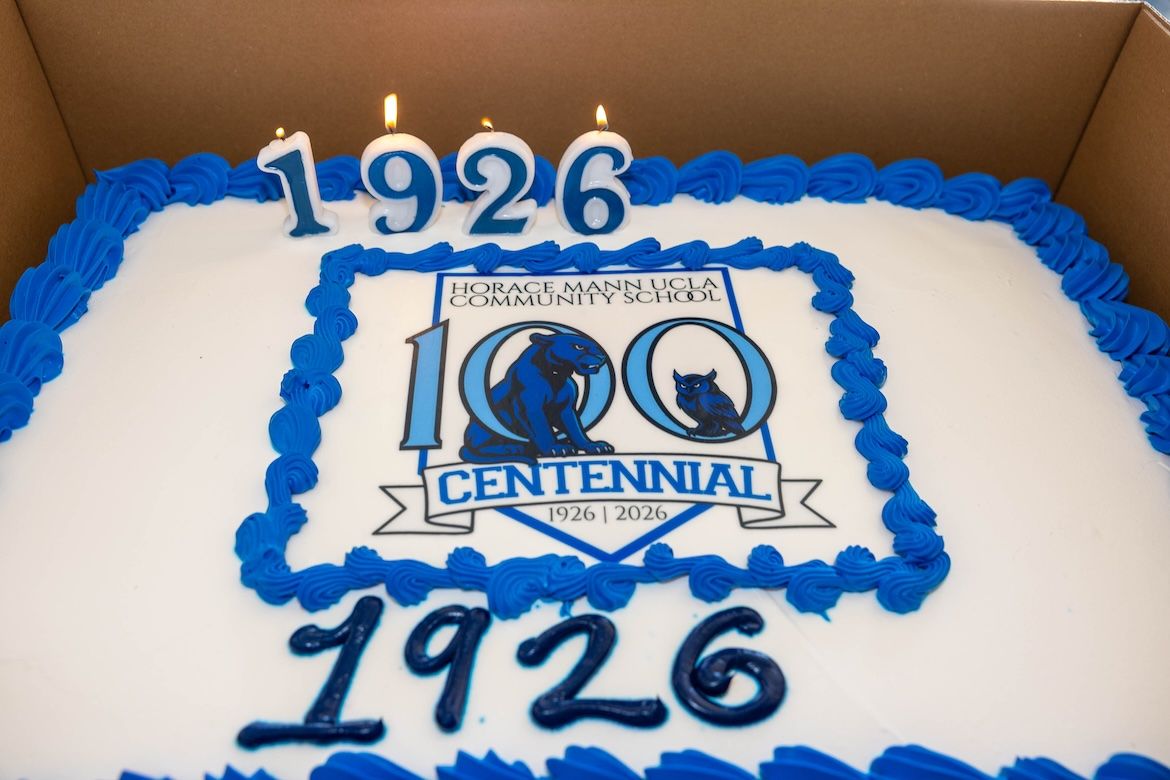 A rectangular cake with blue frosting trim displays “Horace Mann UCLA Community School 100 Centennial 1926–2026.” Four lit candles form “1926” on top, and “1926” is written again in icing below the central centennial logo.