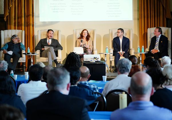 Five panelists seated in white armchairs address the audience