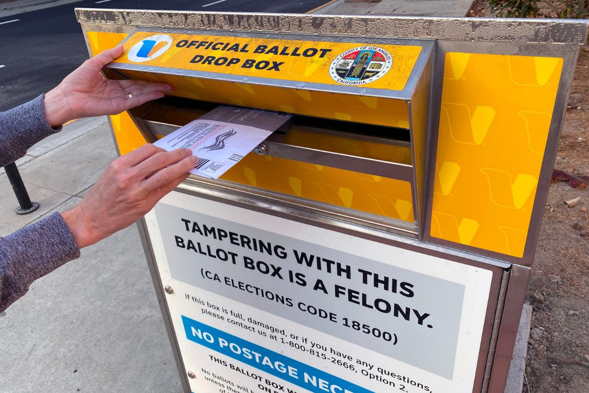Voter holds lid to drop ballot in yellow streetside LA County ballot box