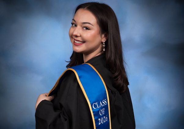 Allana Martinez smiles in a graduation portrait while wearing a black gown and a blue stole reading “Class of 2026.”