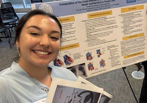 Allana Martinez smiles beside her research poster during a PULSE presentation, holding anatomical diagrams related to her project.