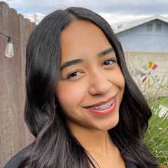 Amaya Ellis, smiling, with long, straight dark hair, photographed outdoors with a wooden fence in the background.