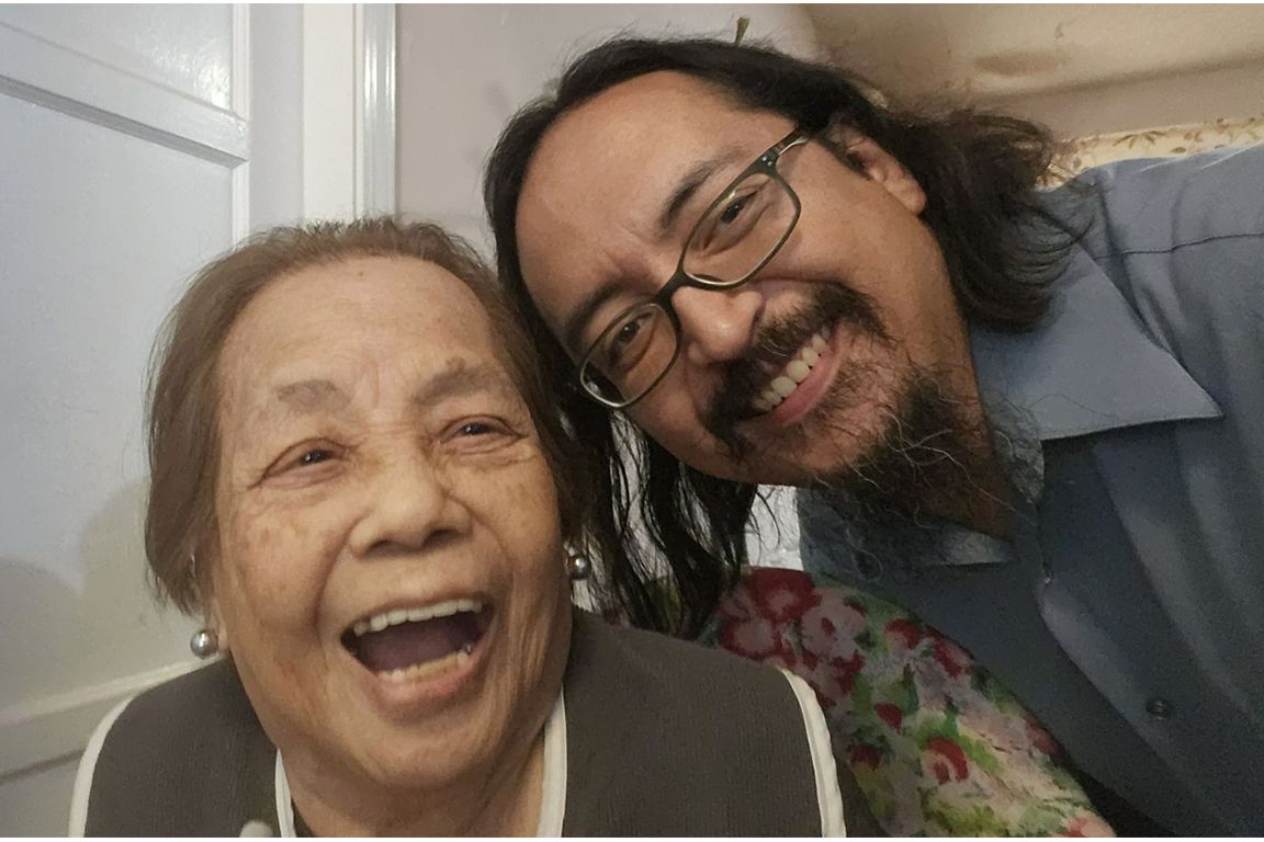 Emmanuel Masongsong takes a selfie with his grandmother, Salome "Mimi" Rili, who is laughing joyfully. Both are smiling broadly indoors.