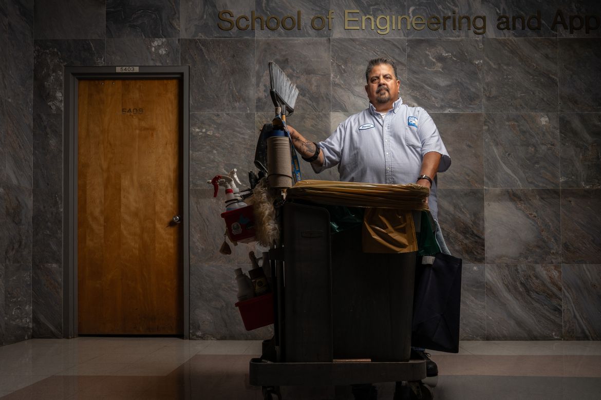 UCLA senior custodian Daniel Estrada stands beside his custodial cart inside UCLA’s School of Engineering, where he has worked maintaining classrooms and campus spaces