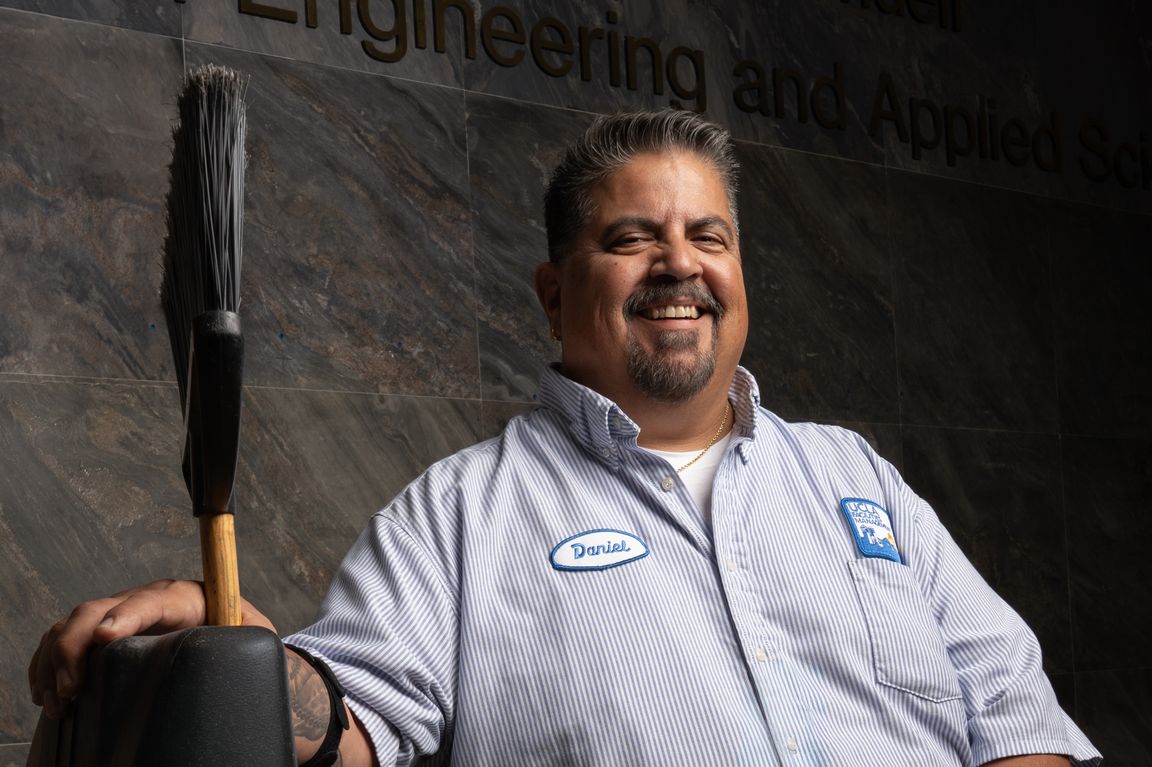 UCLA senior custodian Daniel Estrada smiles beside his custodial equipment inside UCLA’s School of Engineering and Applied Science, where he helps maintain classrooms and campus spaces for students, faculty and staff.