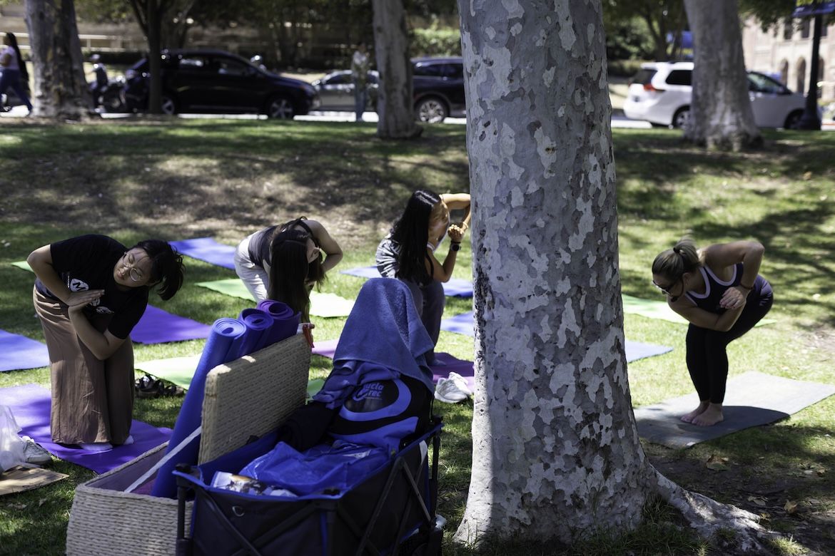 Four Bruins practice yoga on colorful mats beneath trees during the Day of Hope mental health and wellness event on the UCLA campus lawn.