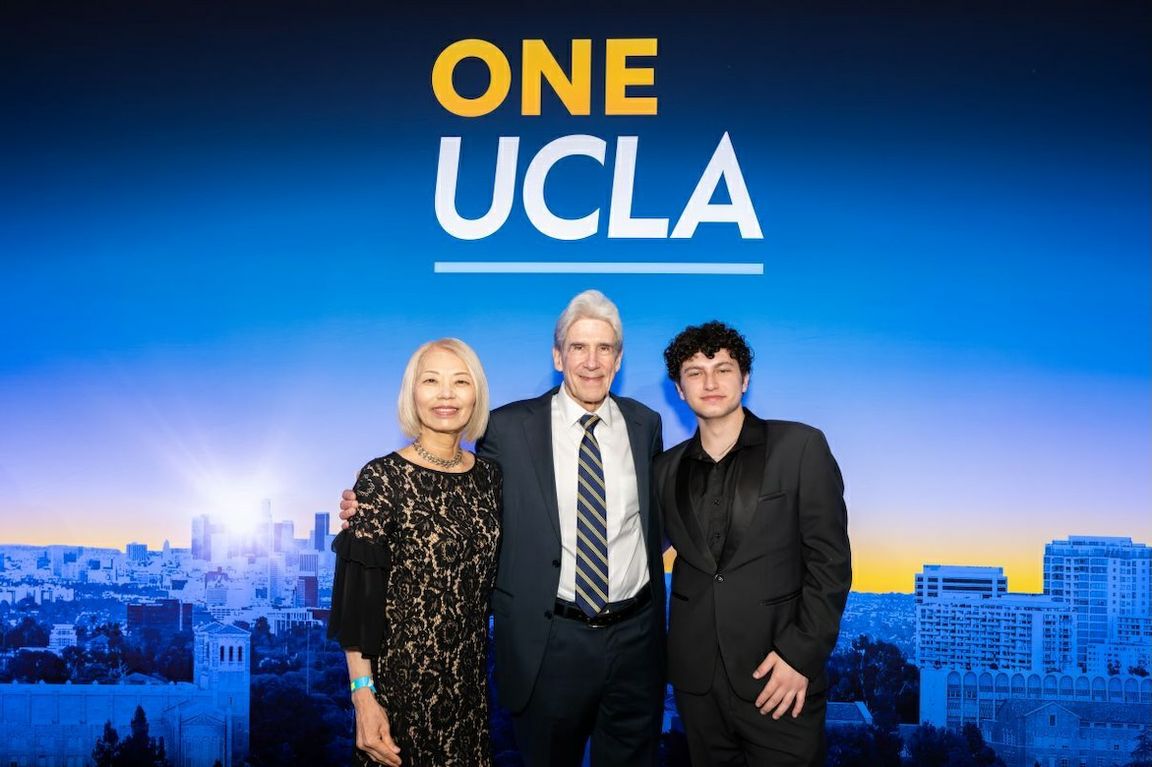 Chancellor Julio Frenk stands at center with a senior member of the graduating class, Mayu Sasame, and one of the youngest, August Maturo, in front of backdrop with One UCLA in yellow and white letters