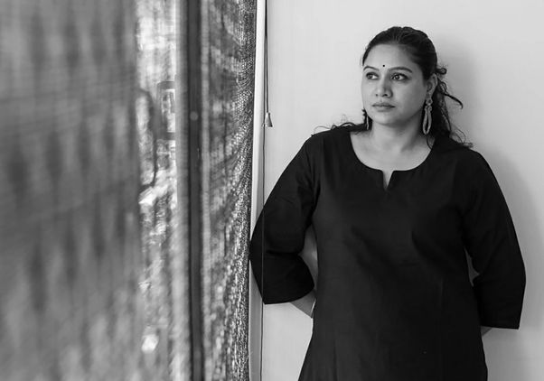 Black-and-white midrange photo of Neha Dixit in dark outfit, leaning against a wall