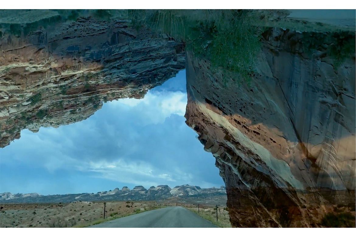 View of desert landscape, sky, road and rocky hills seen through a rock arch overlay