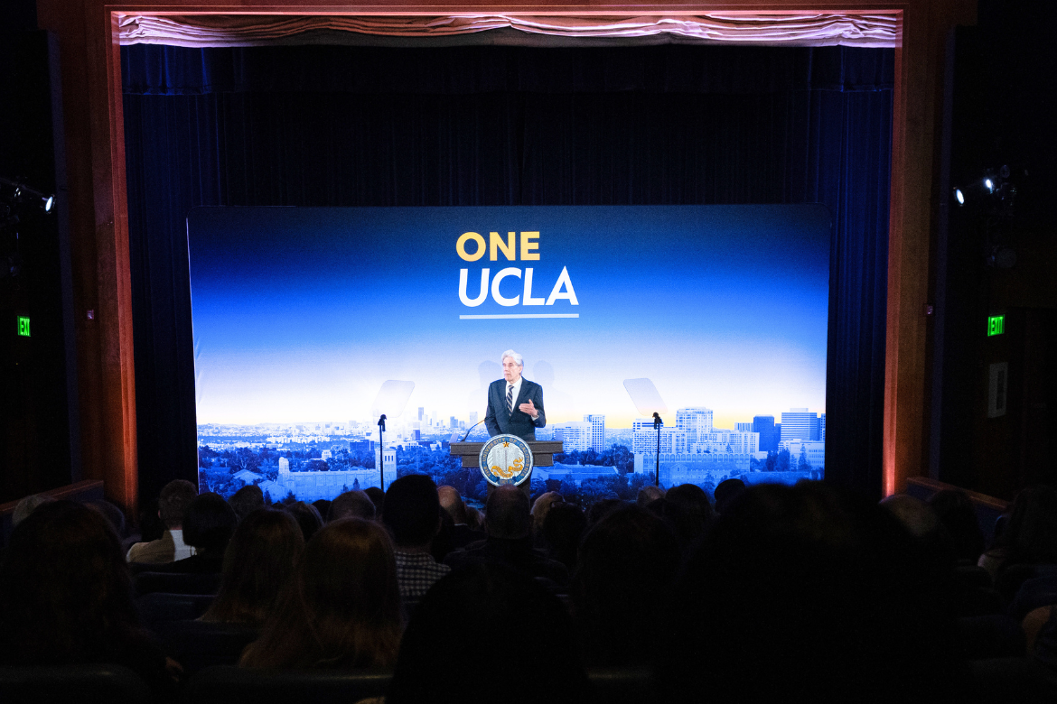 Chancellor Julio Frenk stands in front of auditorium crowd with blue white and yellow UCLA campus backdrop during 2026 State of the Campus address