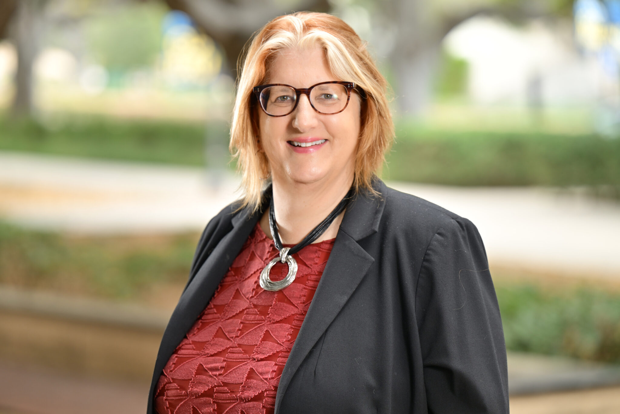 Head-and-shoulders photo of Alexandra Minna Stern wearing red top, black jacket and glasses.