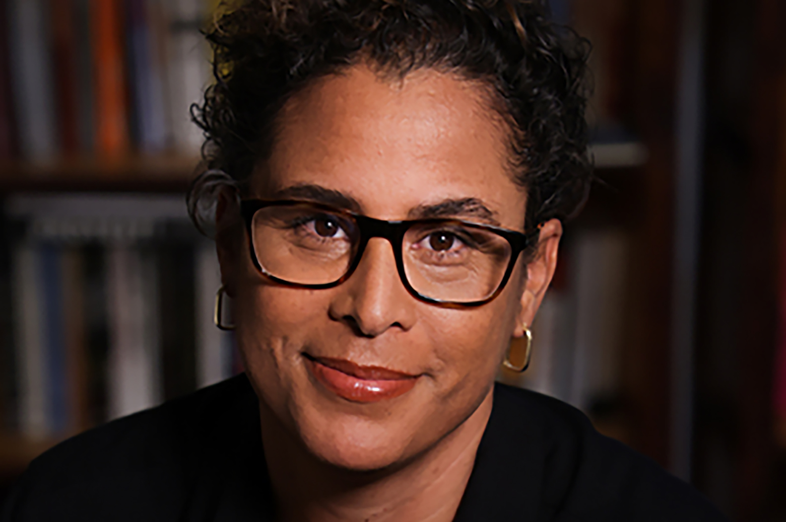 Close-up of Kelly Lytle Hernández, wearing dark top, glasses and earrings.