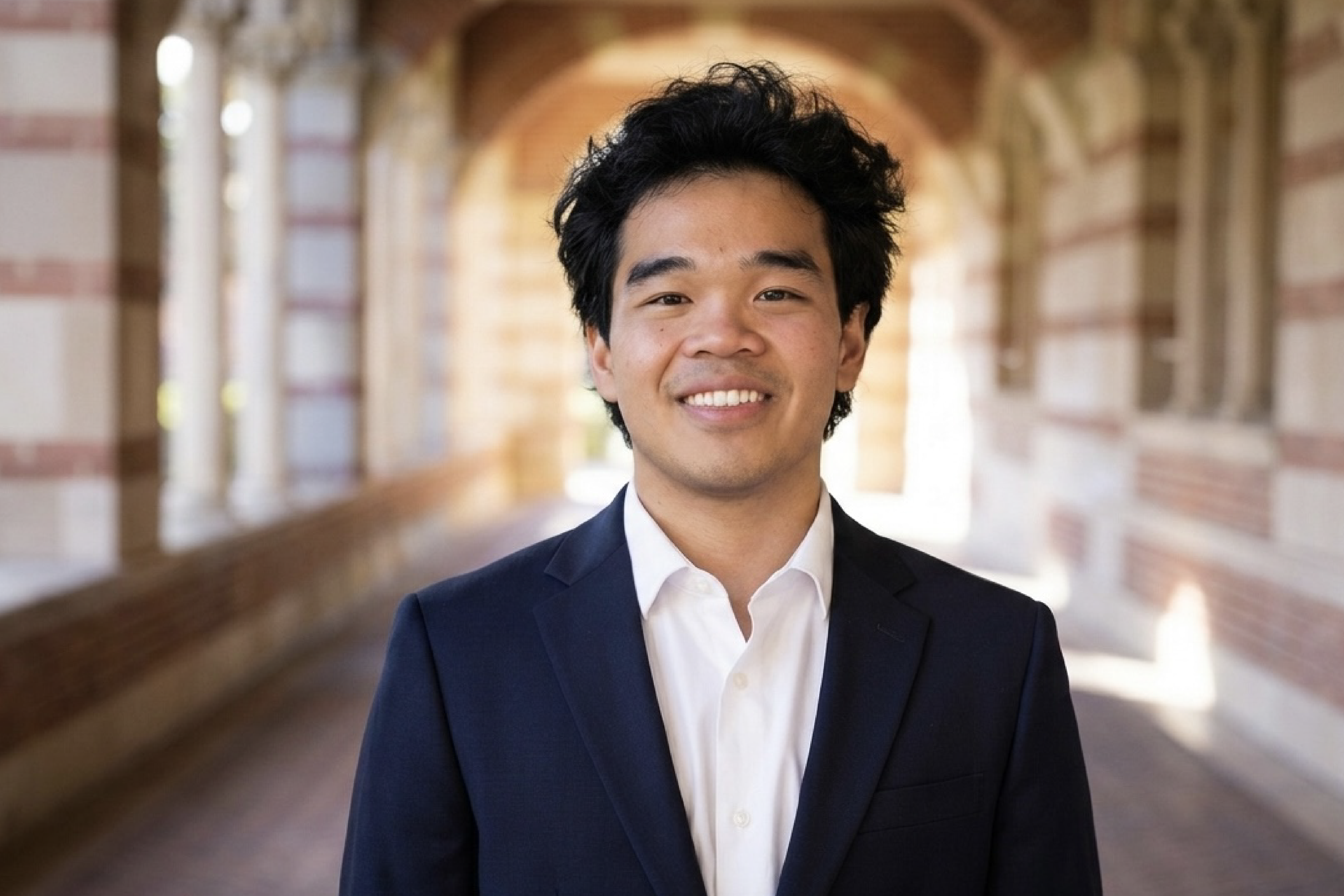 Head-and-shoulders shot of Riley Joe in white button-down and dark blue jacket in Royce Hall portico