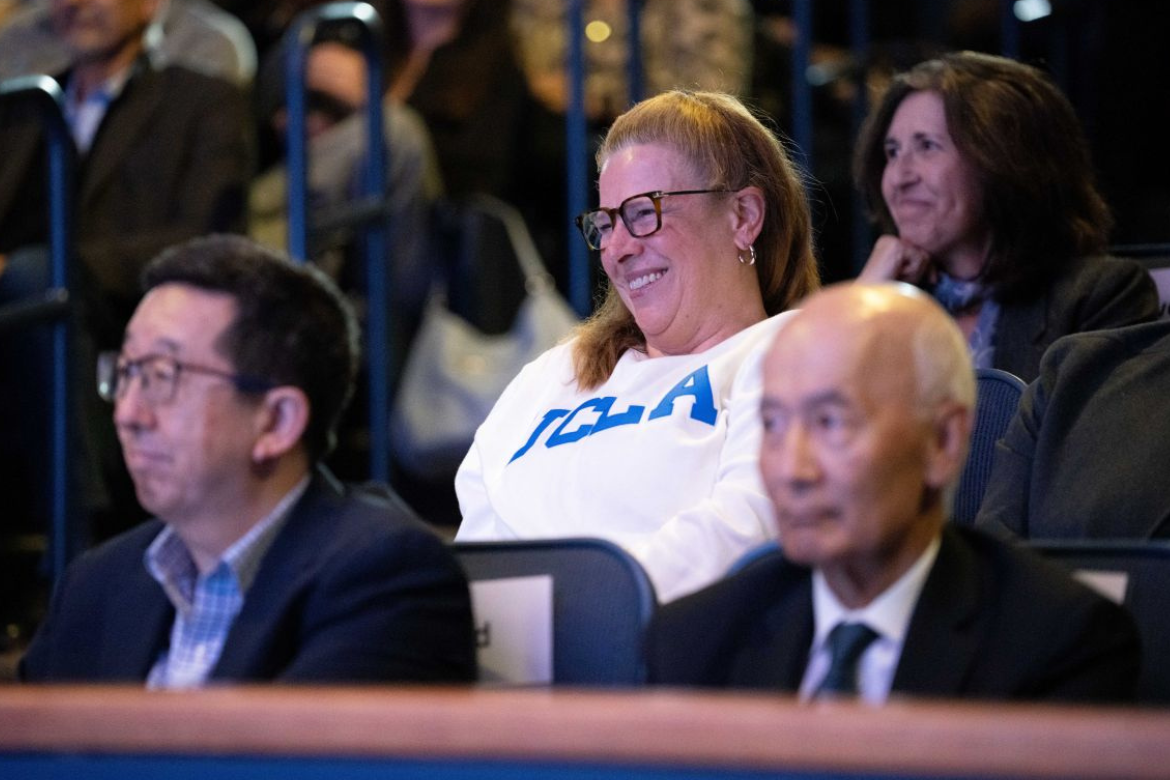 Smiling Cori Close in white sweatshirt and blue UCLA logo sits among the seated crowd during the 2026 State of the Campus address