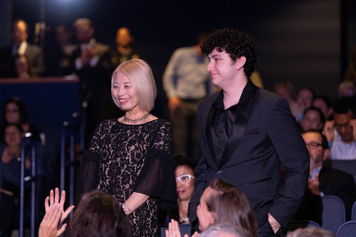 Mayu Sasame in black lace dress stands up in a crowd with August Maturo in dark shirt and jacket during State of the Campus address