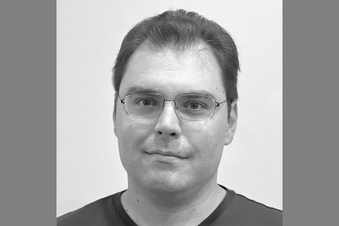 Black-and-white close-up of Thomas Dumitrescu wearing dark T-shirt and glasses