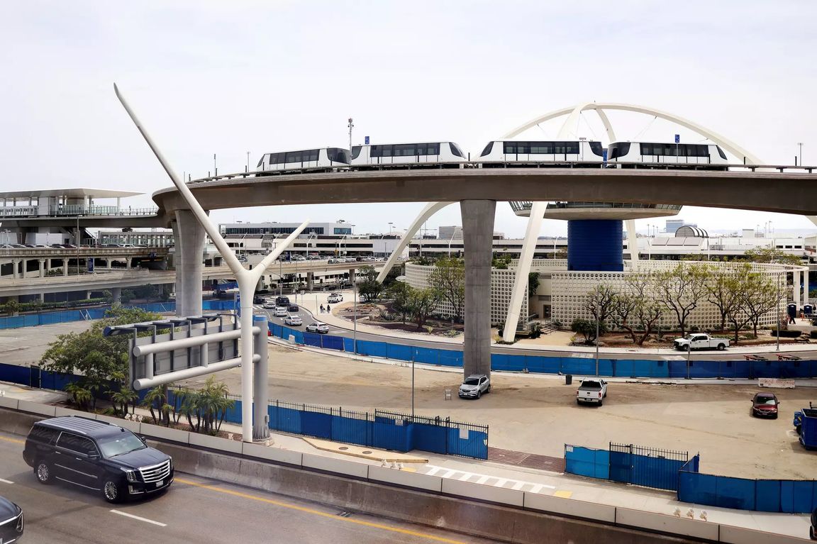 The SkyLink automated train travels along its elevated guideway past the iconic Theme Building at Los Angeles International Airport during testing in April. Airport roadways, terminals and construction areas are visible below the train.