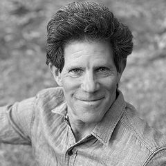 Black-and-white headshot of Larry Smith wearing a button-up shirt, looking at the camera against a blurred outdoor background.