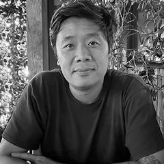 Black-and-white portrait of Ryan Young wearing a dark T-shirt while seated with folded arms, looking at the camera in an outdoor setting.