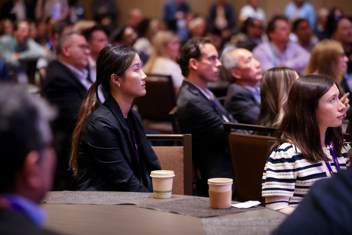 Audience members listen attentively during a UCLA Technology Development Group LABEST conference session. Seated participants face the speaker with focused expressions, while a crowded ballroom of entrepreneurs, researchers, investors and industry leaders fills the background.