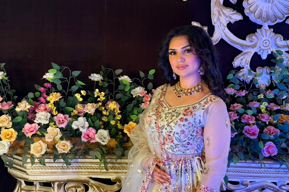 Atithi Multani in traditional garb with a floral pattern and embellishments, standing in front of a railing and flowers