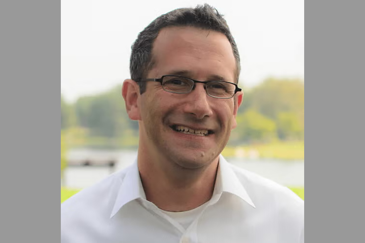 Head-and-shoulders photo of Marc Suchard wearing white button-down and glasses in a park setting.
