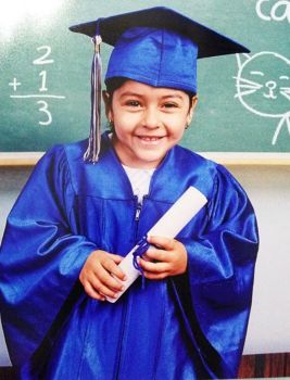 Young Karla Vasquez in blue graduation robe and holding white rolled paper diploma
