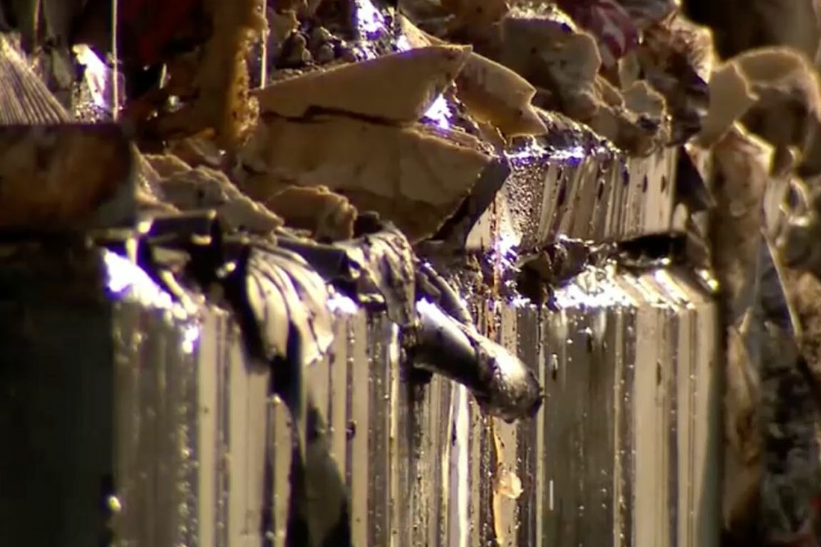 Close-up of a corrugated metal surface covered in charred, melted debris with dripping residue.