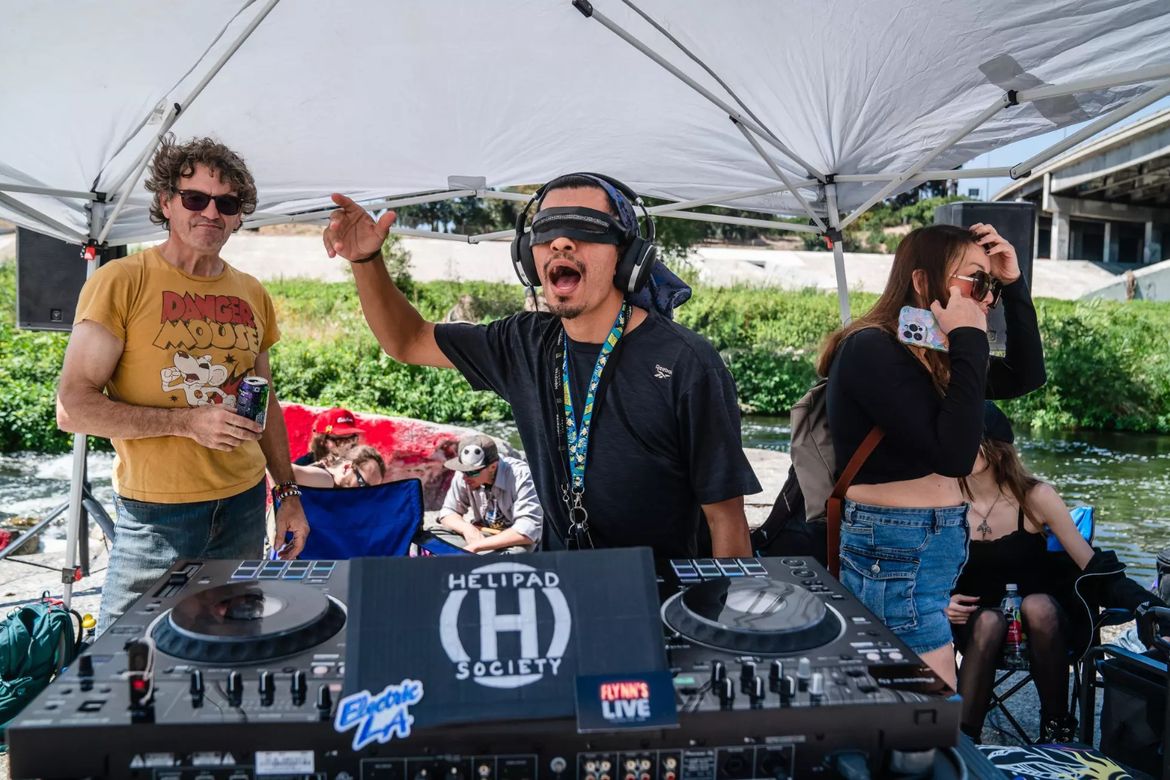 DJ Brawl holds right arm up in the air as he spins behind a record turntable