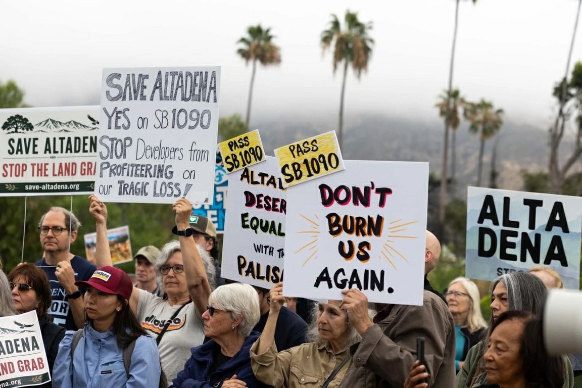 People hold signs supporting California Senate Bill 1090 during a community rally in Altadena in June. Several signs advocate for protecting the community from post-fire redevelopment and land speculation.