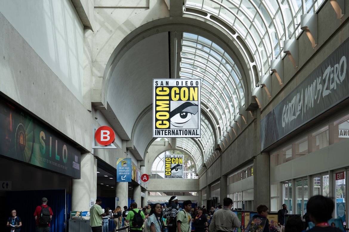 Large Comic-Con International banners hang from the vaulted ceiling inside the San Diego Convention Center as attendees move through the concourse.