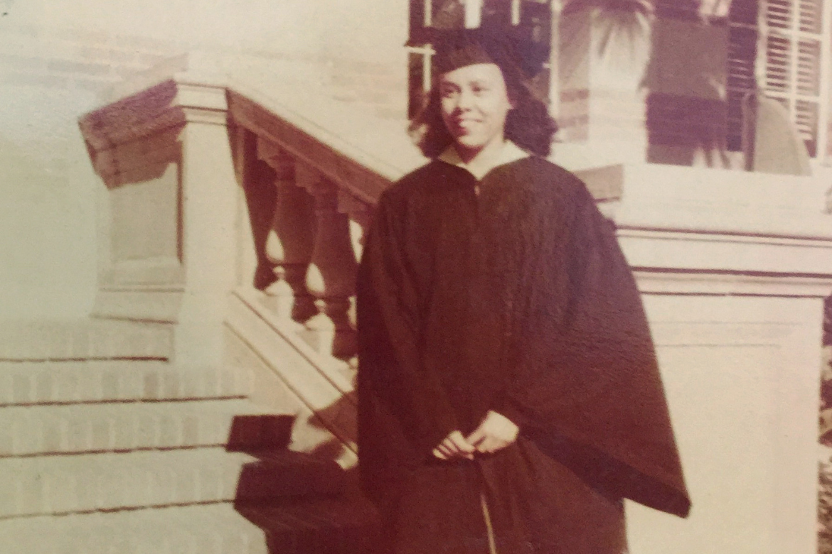 Black-and-white photo of Betye Saar standing on brick steps in graduation cap and gown
