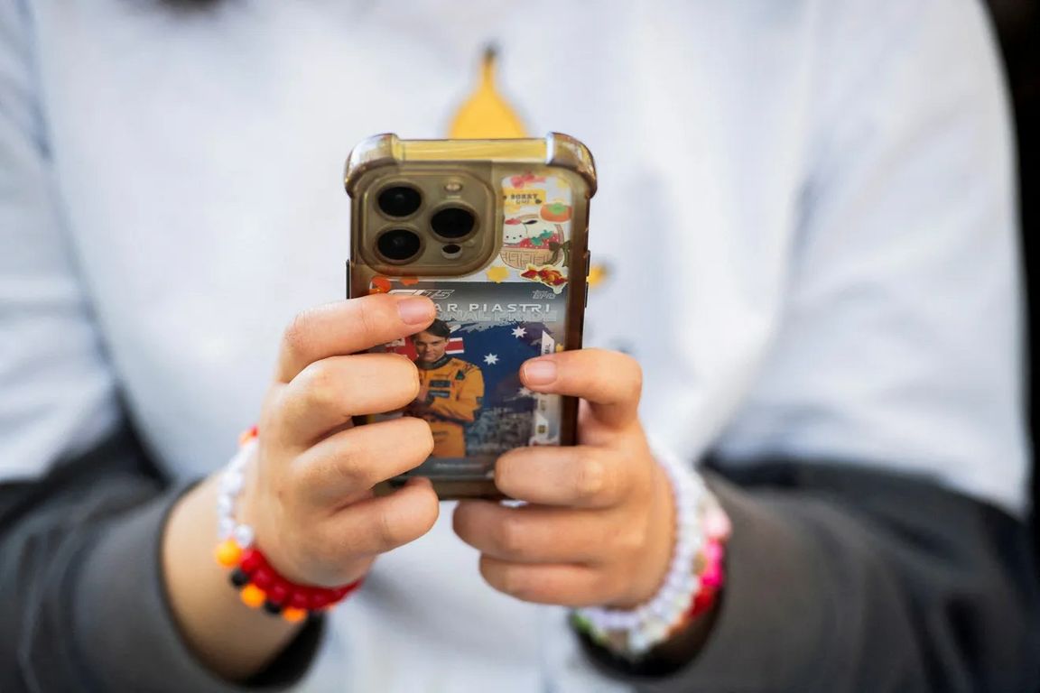 A young person holds a smartphone decorated with stickers and a Formula 1 trading card.