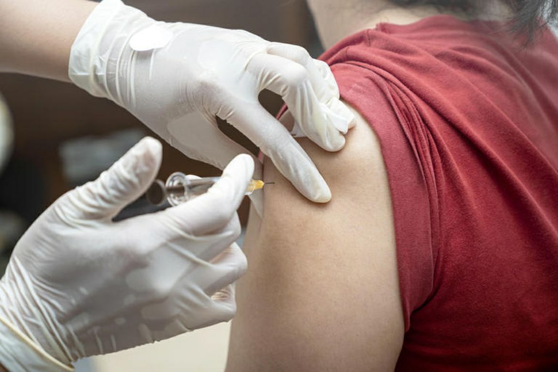 A health care worker wearing gloves administers an injection into a person’s upper arm.