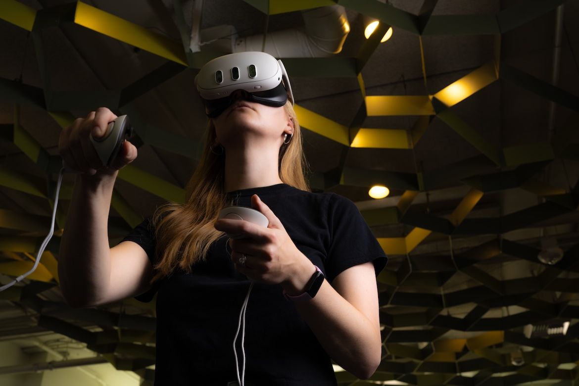 A student wearing a virtual reality headset uses handheld controllers to explore a digital environment at UCLA.