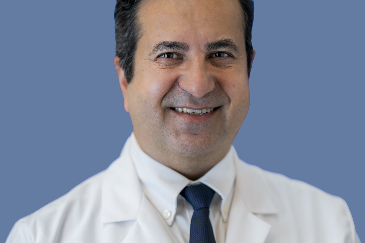 close  Head-and-shoulders photo of Bijan Najafi wearing a white lab coat and dark tie, photographed against a blue background.