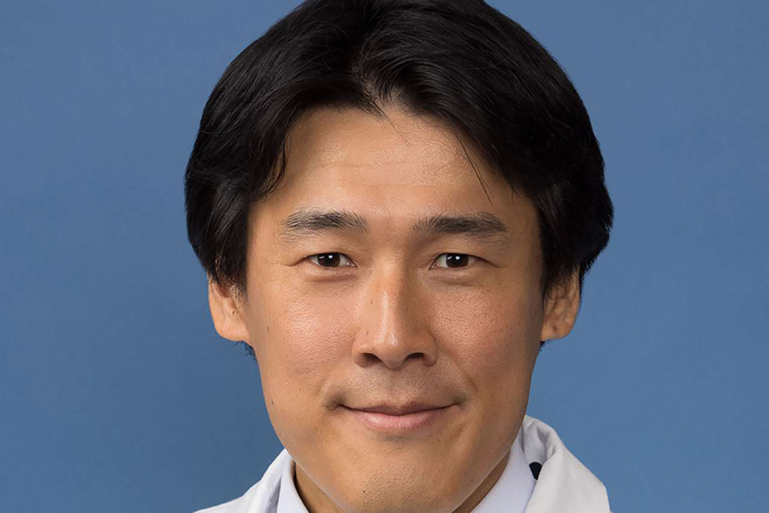Close-up of Naoki Kaneko wearing a white coat against a blue background.