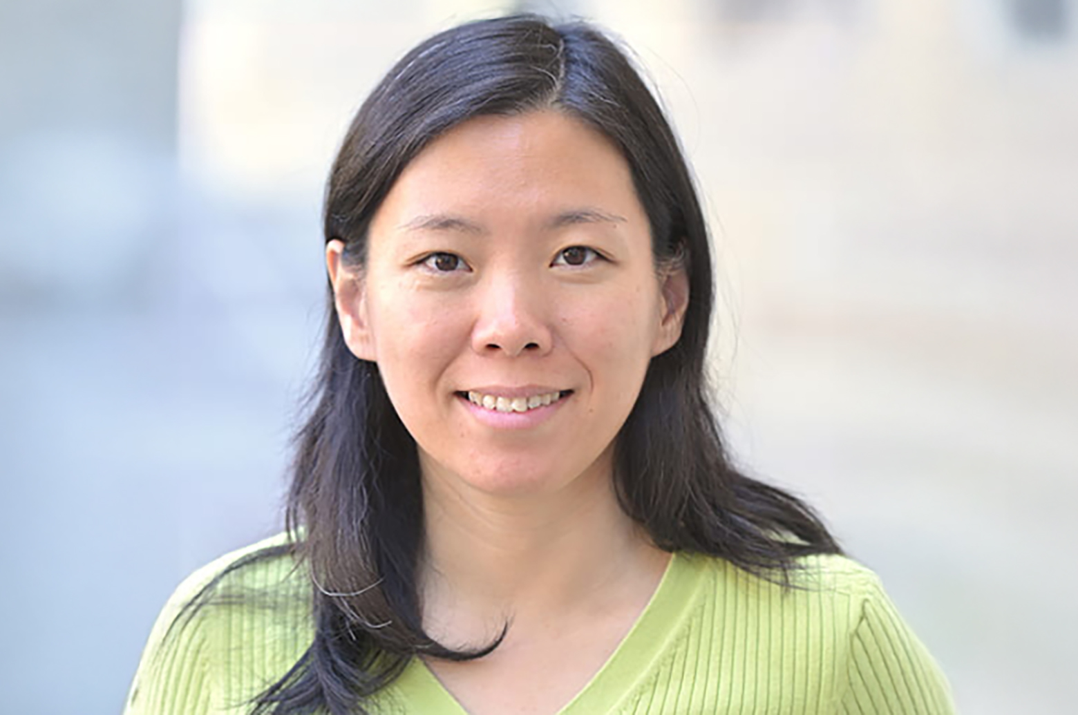 Portrait of Wei Wang wearing a light green sweater, standing outdoors against a softly blurred background.