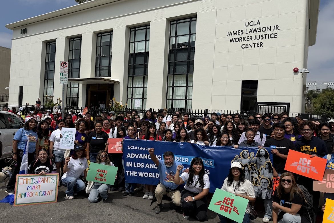 A large group of workers and supporters gathers outside UCLA’s James Lawson Jr. Worker Justice Center, holding signs and a UCLA Labor Center banner calling for worker justice and immigrant rights.